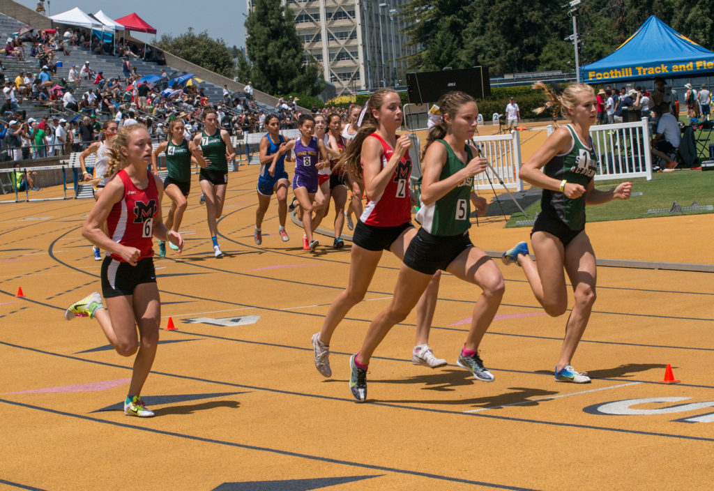 Athlete prepares for pole vault on a track with others watching.