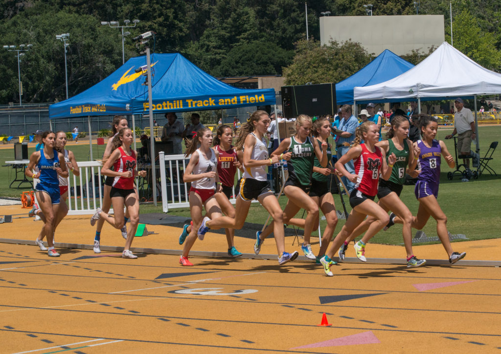 Athlete prepares for pole vault on a track with others watching.