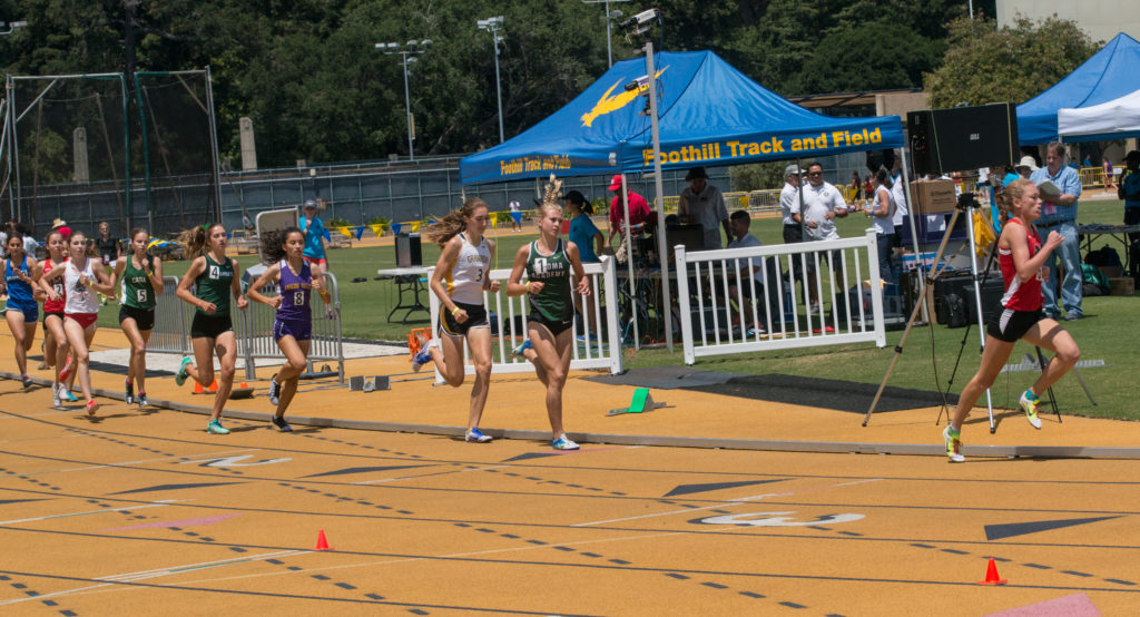 Athlete prepares for pole vault on a track with others watching.