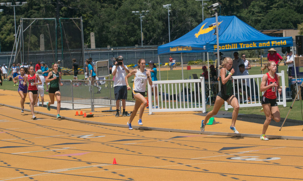 Athlete prepares for pole vault on a track with others watching.