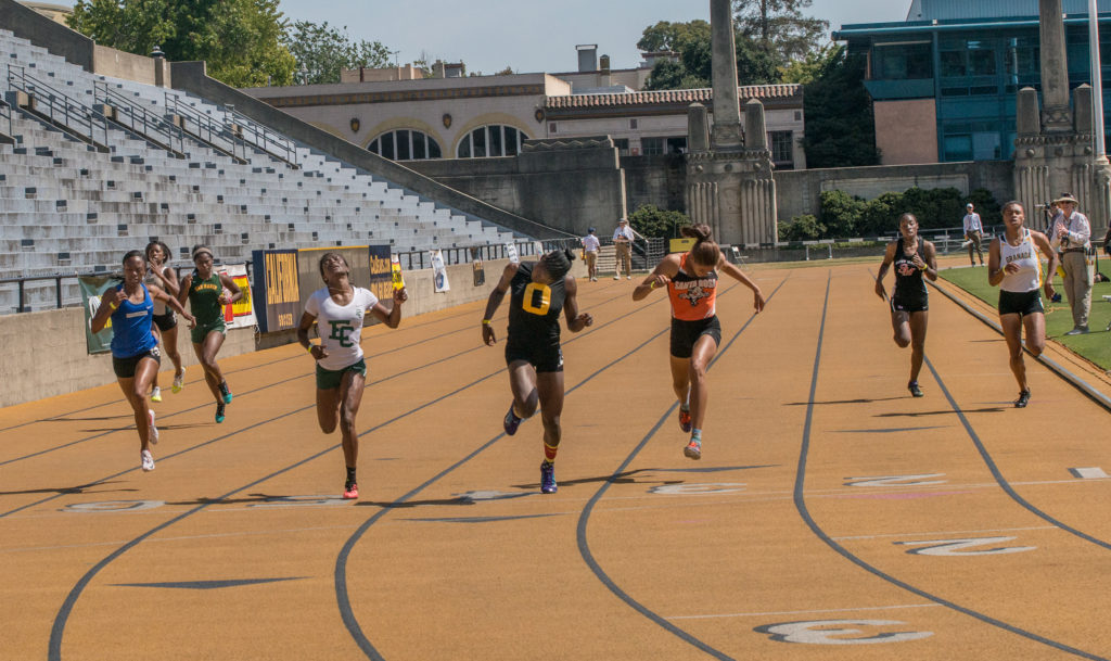 Athlete prepares for pole vault on a track with others watching.