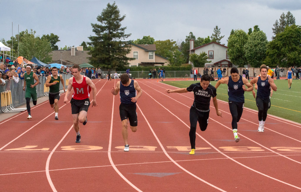 Athlete prepares for pole vault on a track with others watching.