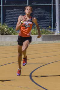 Athlete prepares for pole vault on a track with others watching.