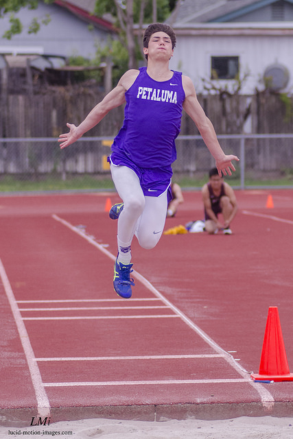 Athlete prepares for pole vault on a track with others watching.