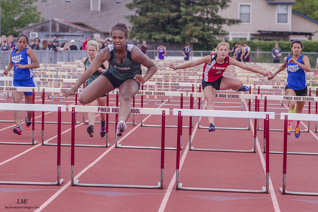 Athlete prepares for pole vault on a track with others watching.