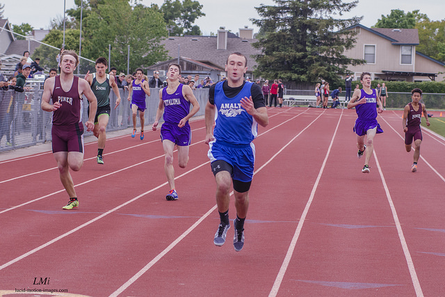 Athlete prepares for pole vault on a track with others watching.