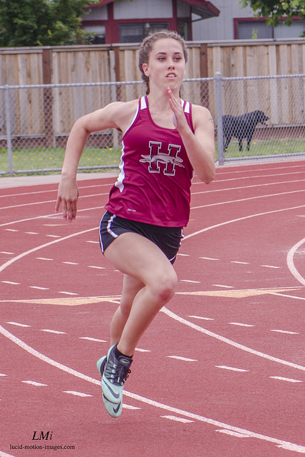 Athlete prepares for pole vault on a track with others watching.