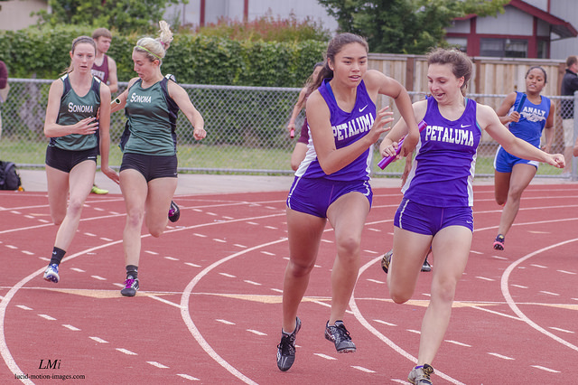 Athlete prepares for pole vault on a track with others watching.