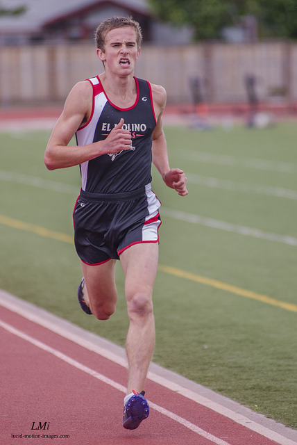 Athlete prepares for pole vault on a track with others watching.