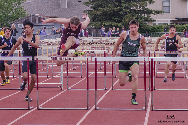 Athlete prepares for pole vault on a track with others watching.