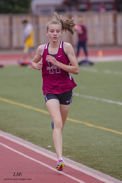 Athlete prepares for pole vault on a track with others watching.