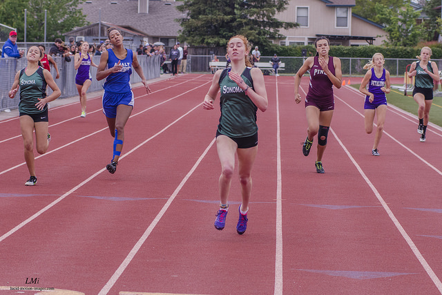 Athlete prepares for pole vault on a track with others watching.
