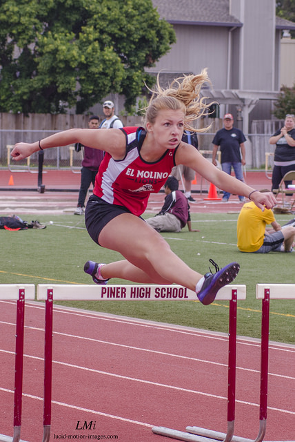 Athlete prepares for pole vault on a track with others watching.