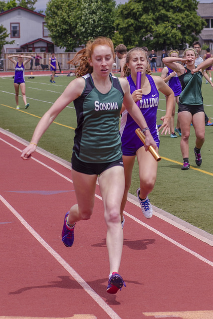 Athlete prepares for pole vault on a track with others watching.