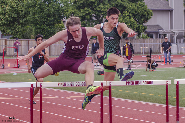 Athlete prepares for pole vault on a track with others watching.