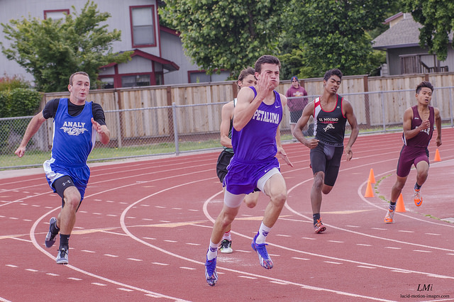 Athlete prepares for pole vault on a track with others watching.