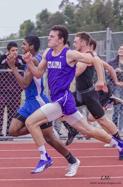 Athlete prepares for pole vault on a track with others watching.