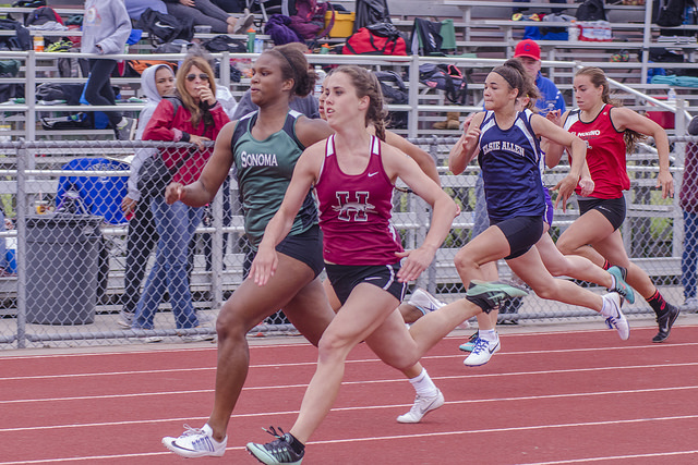 Athlete prepares for pole vault on a track with others watching.