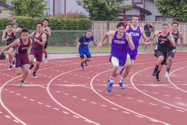 Athlete prepares for pole vault on a track with others watching.