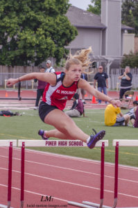Athlete prepares for pole vault on a track with others watching.