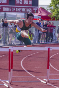 Athlete prepares for pole vault on a track with others watching.
