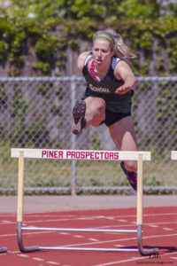 Athlete prepares for pole vault on a track with others watching.