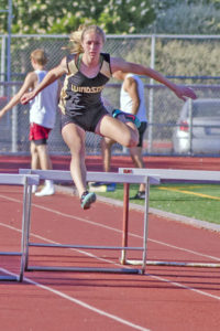 Athlete prepares for pole vault on a track with others watching.