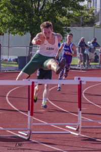 Athlete prepares for pole vault on a track with others watching.