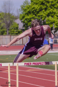 Athlete prepares for pole vault on a track with others watching.