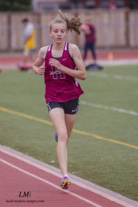 Athlete prepares for pole vault on a track with others watching.