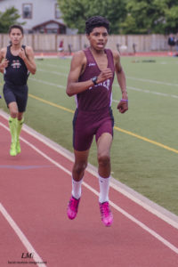 Athlete prepares for pole vault on a track with others watching.