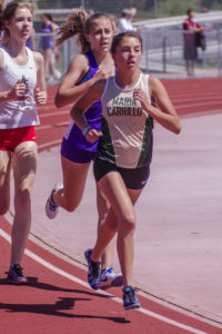 Athlete prepares for pole vault on a track with others watching.