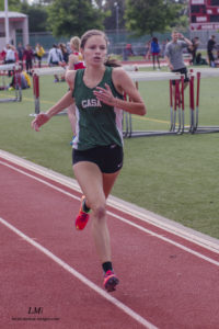 Athlete prepares for pole vault on a track with others watching.