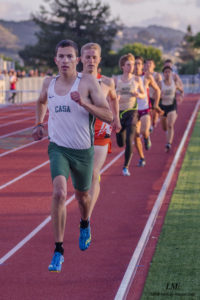 Athlete prepares for pole vault on a track with others watching.