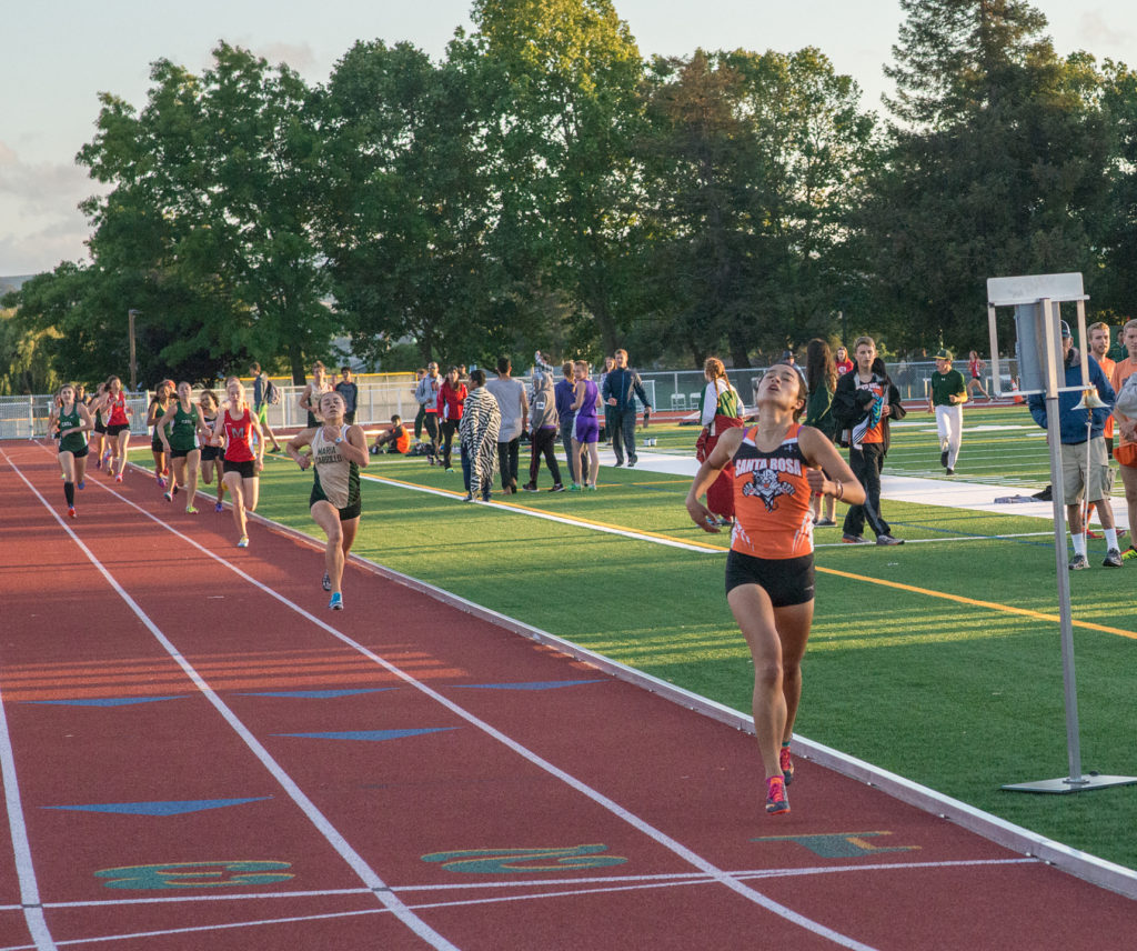 Athlete prepares for pole vault on a track with others watching.