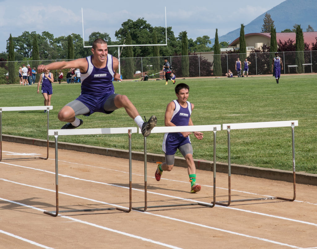 Athlete prepares for pole vault on a track with others watching.