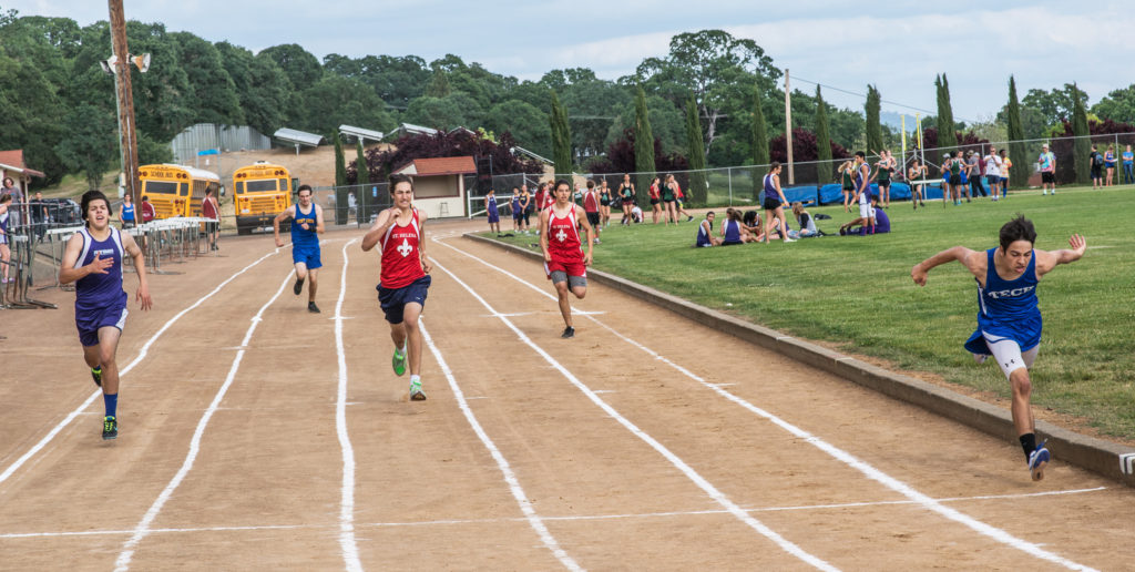 Athlete prepares for pole vault on a track with others watching.