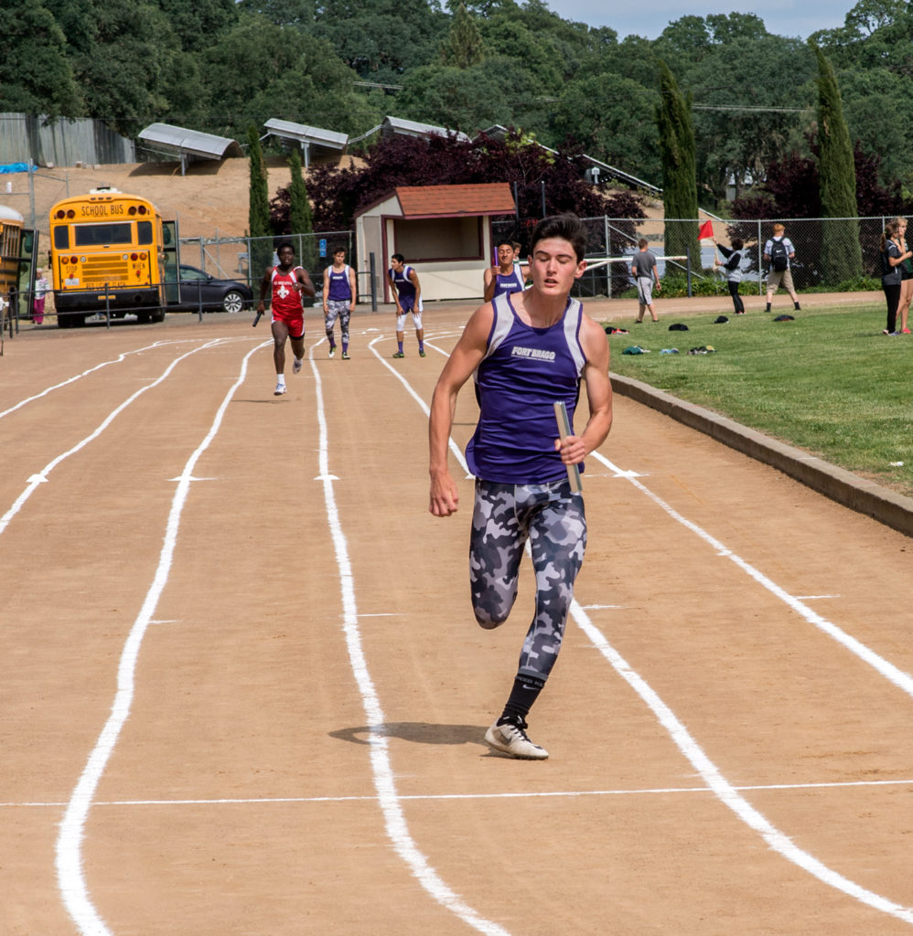 Athlete prepares for pole vault on a track with others watching.