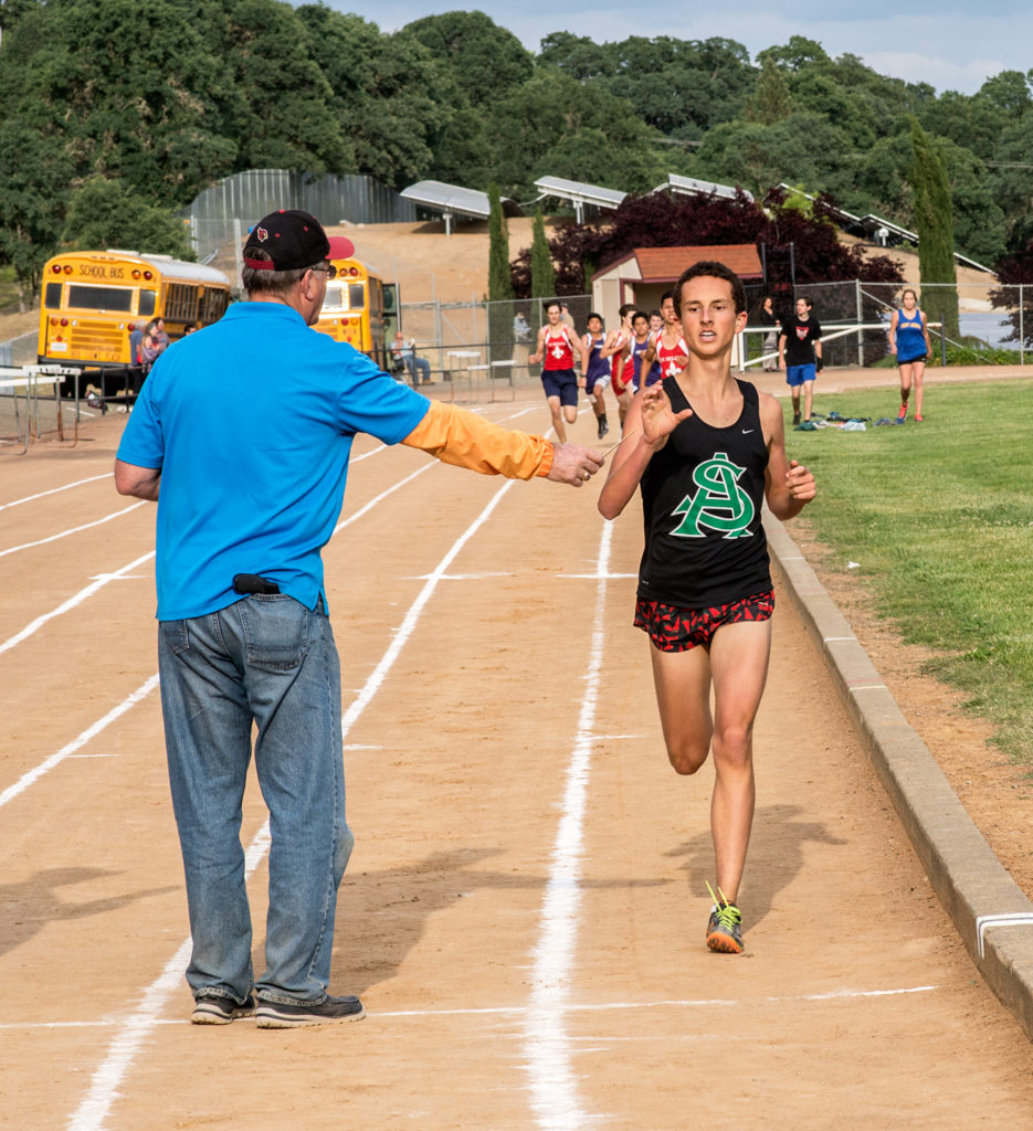 Athlete prepares for pole vault on a track with others watching.