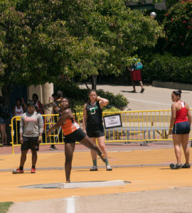 Athlete prepares for pole vault on a track with others watching.