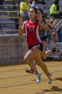 Athlete prepares for pole vault on a track with others watching.