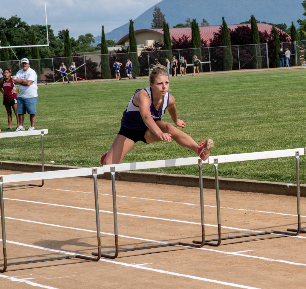 Athlete prepares for pole vault on a track with others watching.