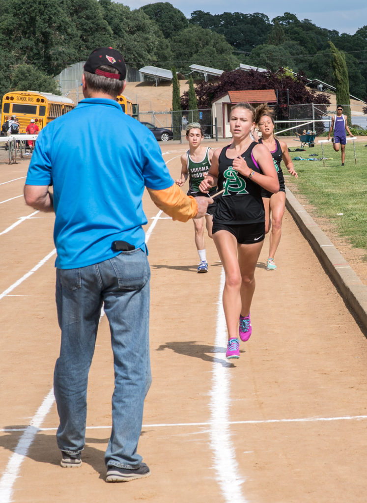 Athlete prepares for pole vault on a track with others watching.
