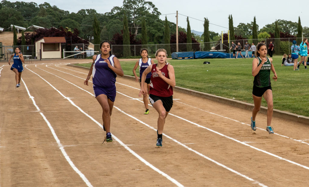 Athlete prepares for pole vault on a track with others watching.