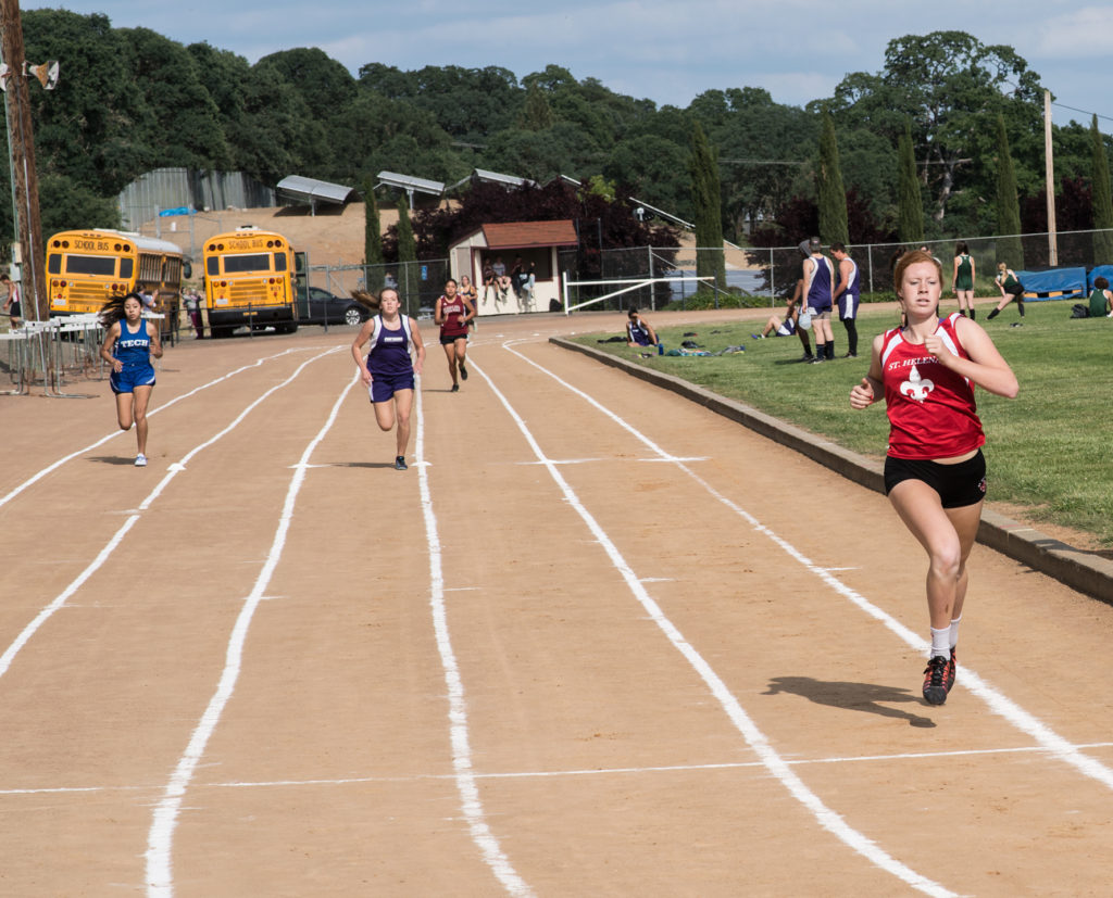 Athlete prepares for pole vault on a track with others watching.