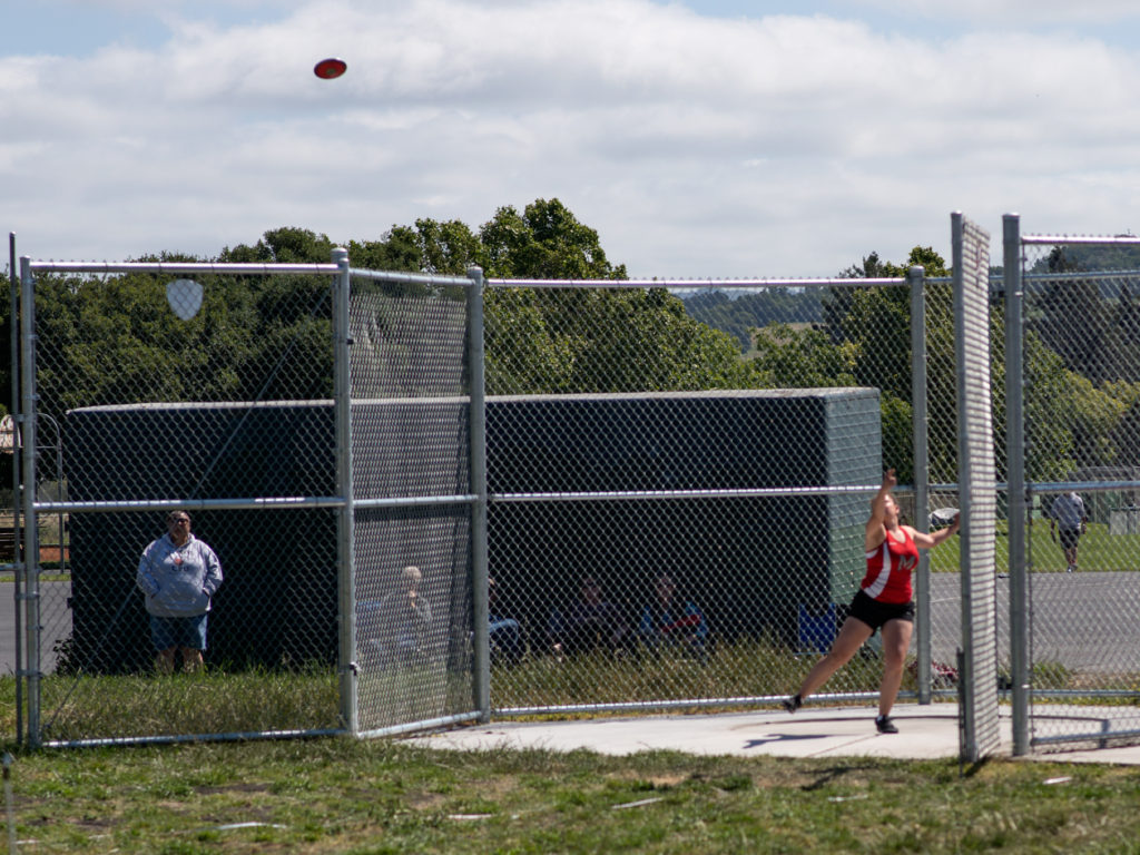 Athlete prepares for pole vault on a track with others watching.