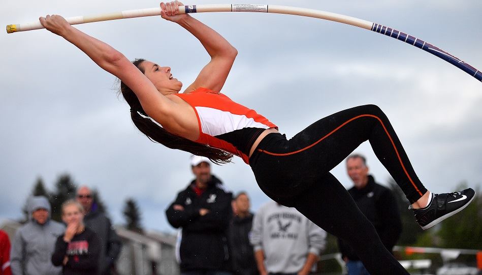 Athlete prepares for pole vault on a track with others watching.