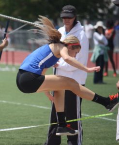 Athlete prepares for pole vault on a track with others watching.