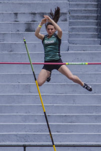 Athlete prepares for pole vault on a track with others watching.