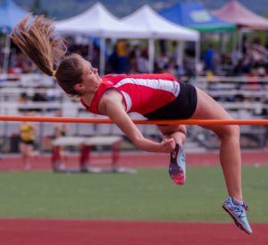Athlete prepares for pole vault on a track with others watching.